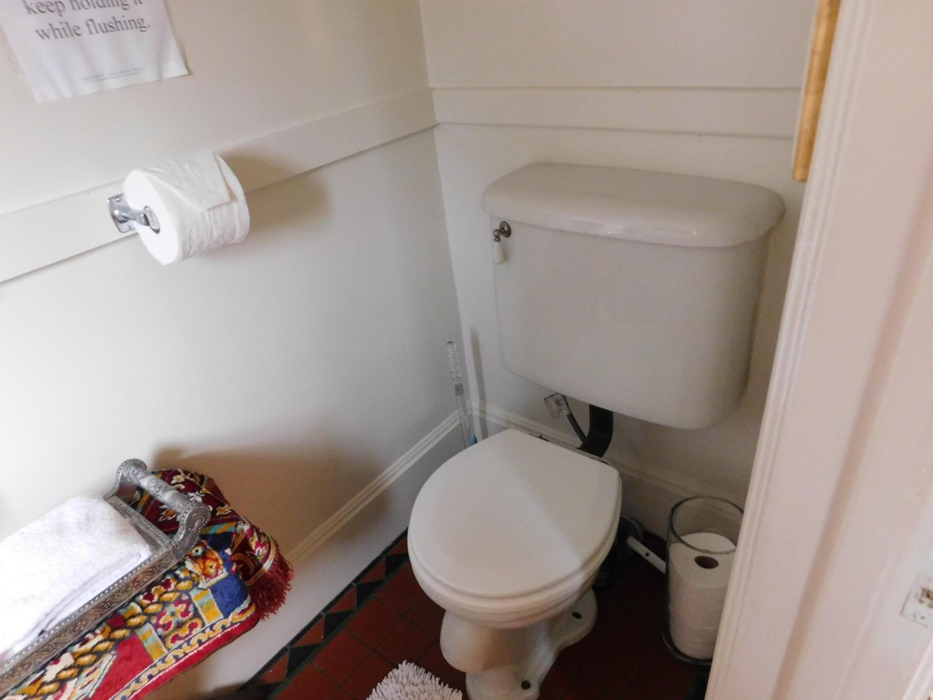 A small, compact bathroom with a toilet, a toilet paper holder, and a trash bin.