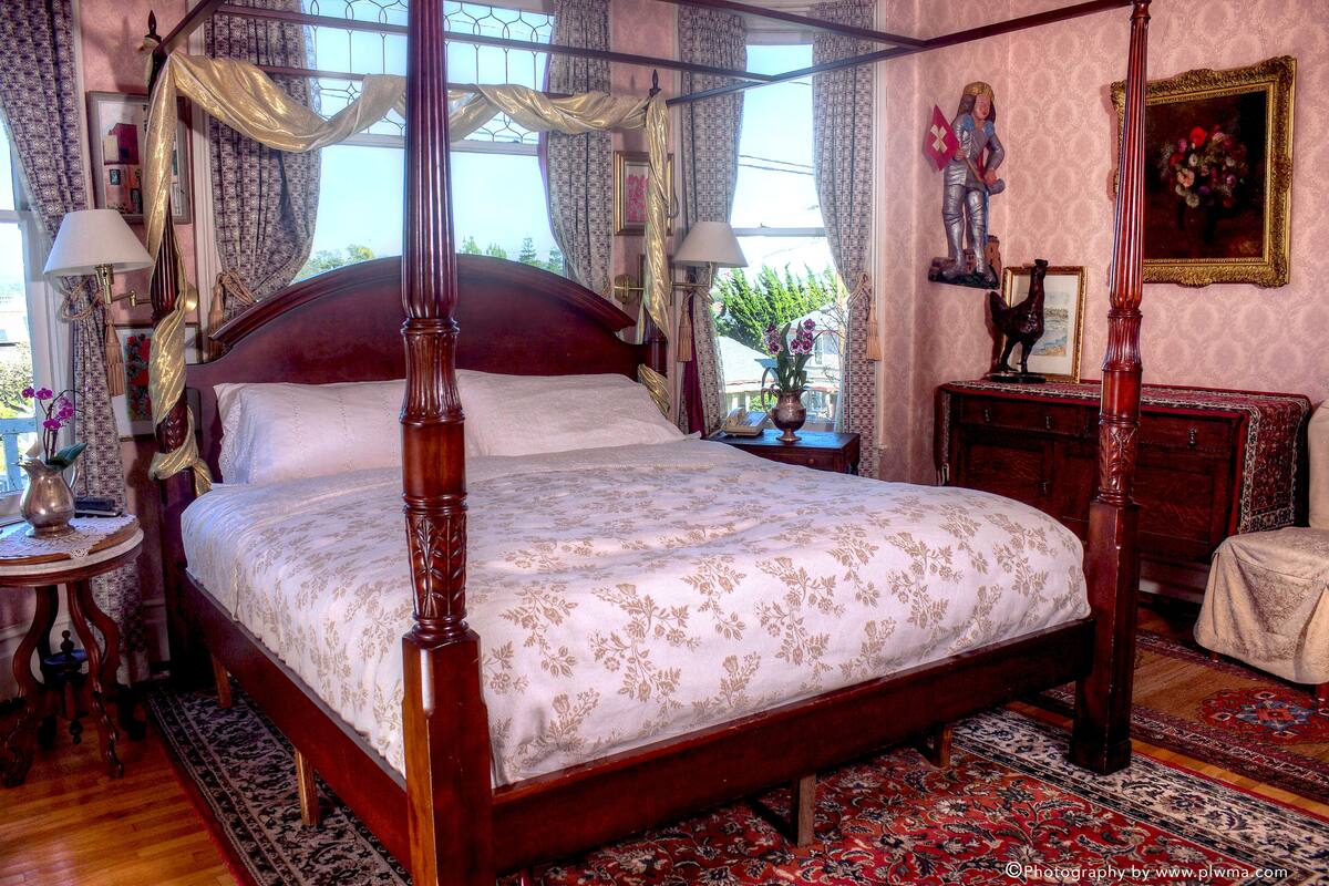 A four-poster canopy bed with a floral bedspread, a nightstand with a lamp, and a dresser with a mirror.