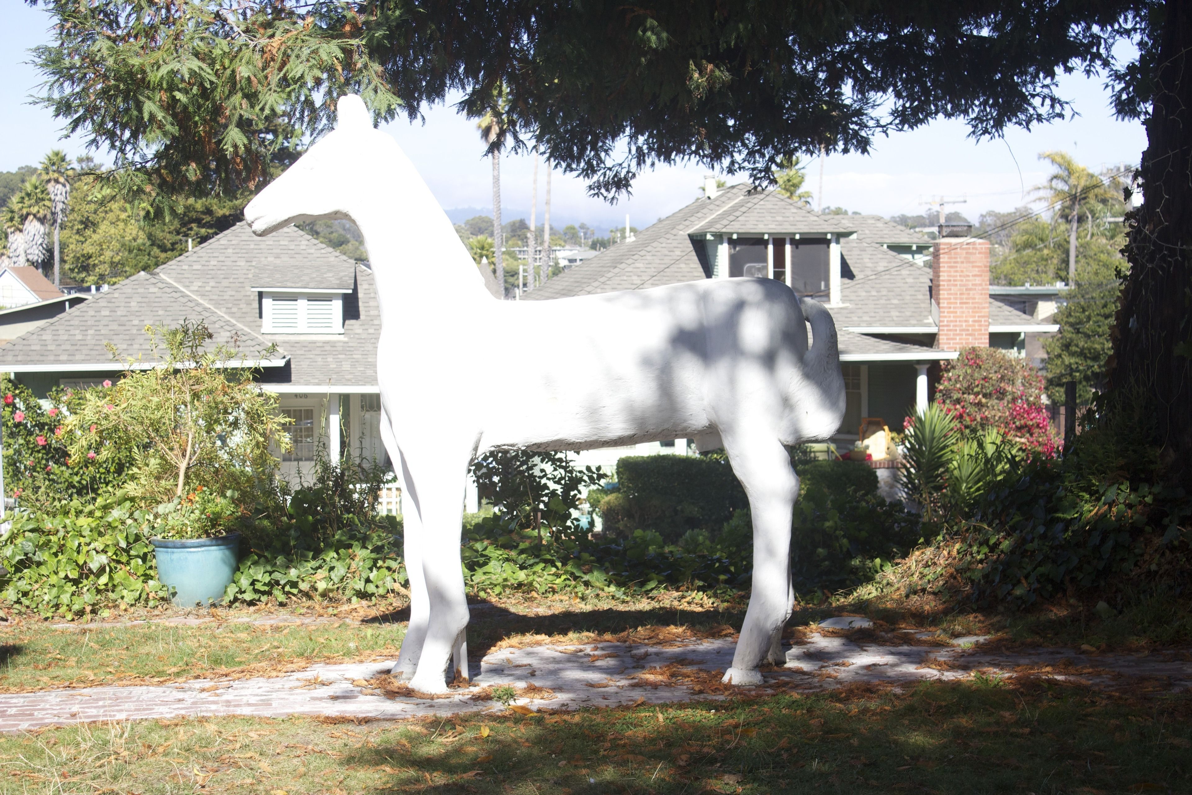 Eine weiße Pferdestatue in einem Garten, im Hintergrund ein Haus.