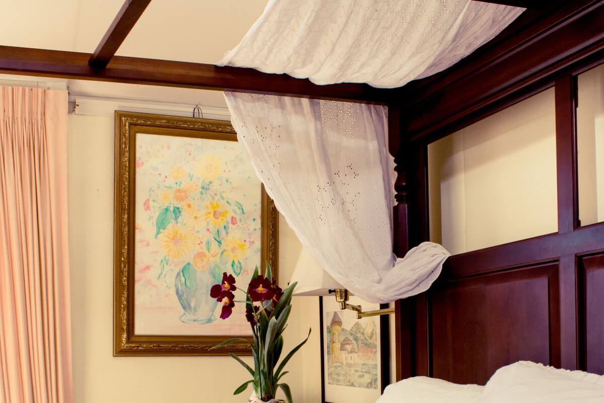 A bedroom with a canopy bed, a vase with flowers, and framed artwork on the wall.