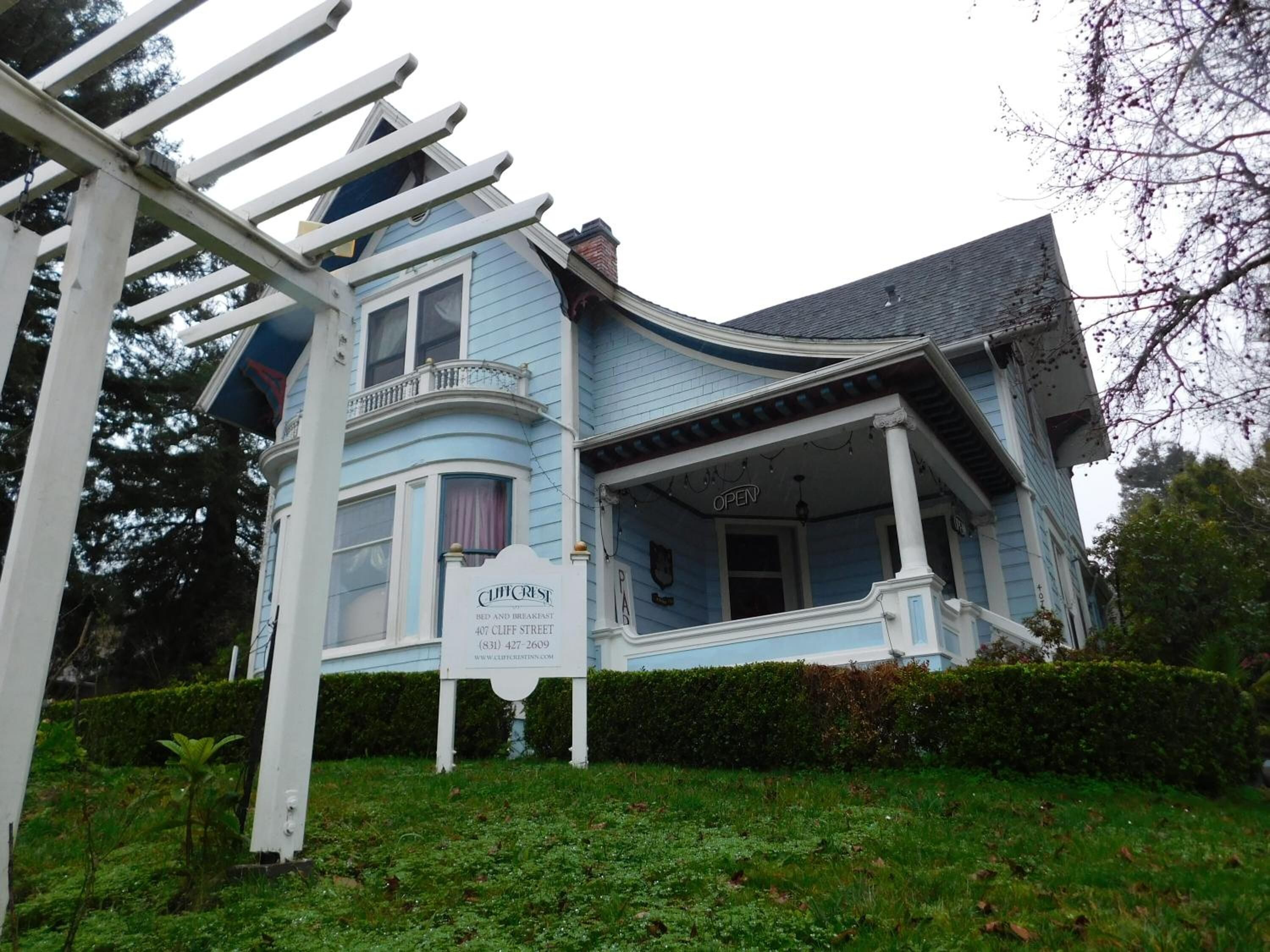A blue Victorian-style house with a porch, a signboard, and a garden.