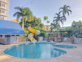 Una piscina con tobogán, rodeada de palmeras y un edificio de techo azul.