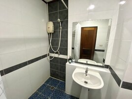 A bathroom with a white sink, a mirror, a shower with a handheld showerhead, and tiled walls.