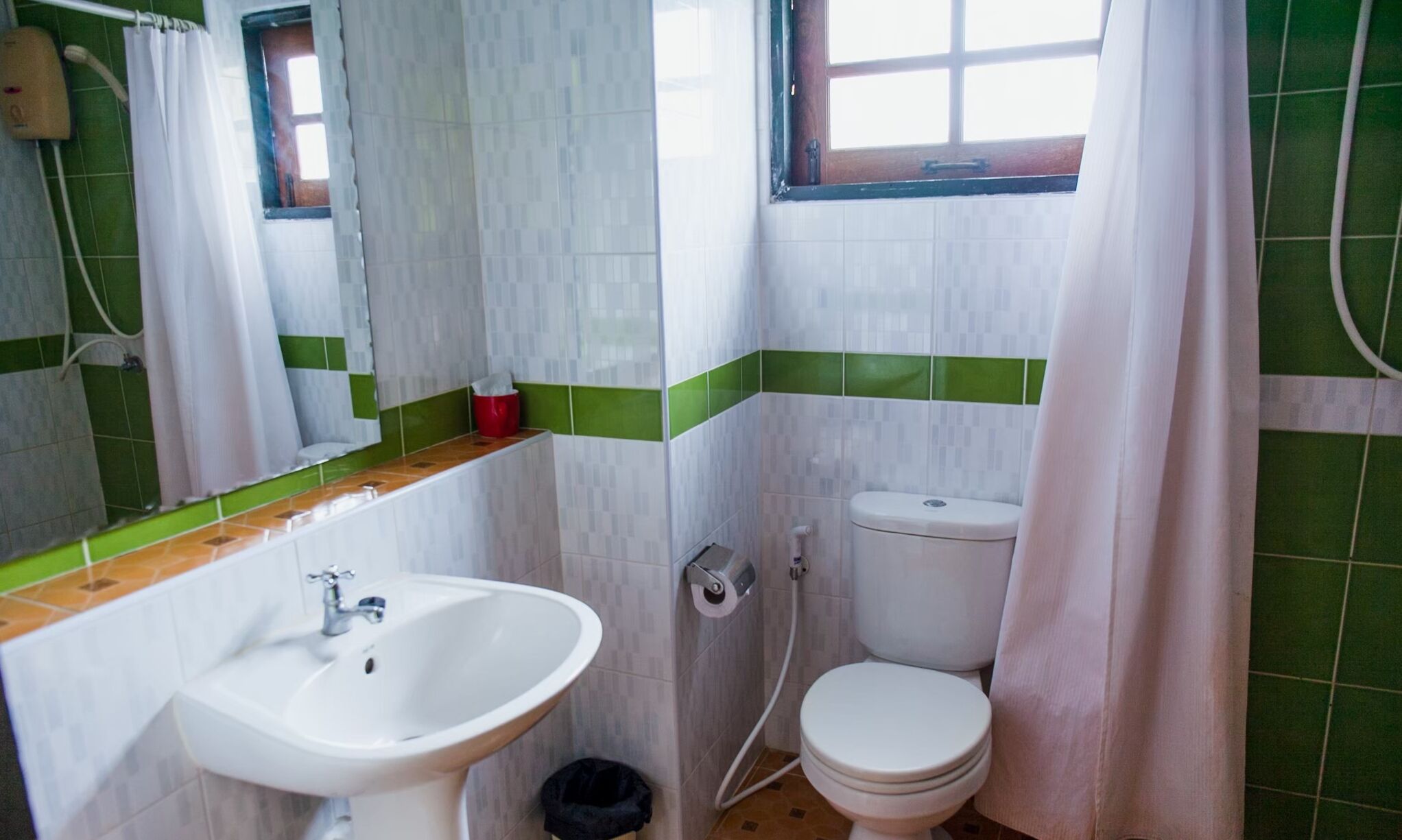 A small bathroom with a sink, toilet, and a window with a curtain.