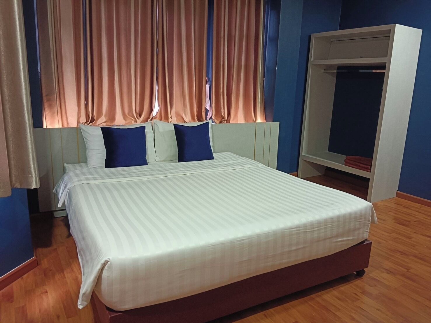 A bed with a white mattress and striped bedding, a headboard with blue and white pillows, and a wardrobe with a mirror.