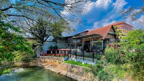 Ein Restaurant am Flussufer mit Außenbereich, Steinstufen, die zum Wasser hinabführen, und Blick auf ein Gebäude im Hintergrund.
