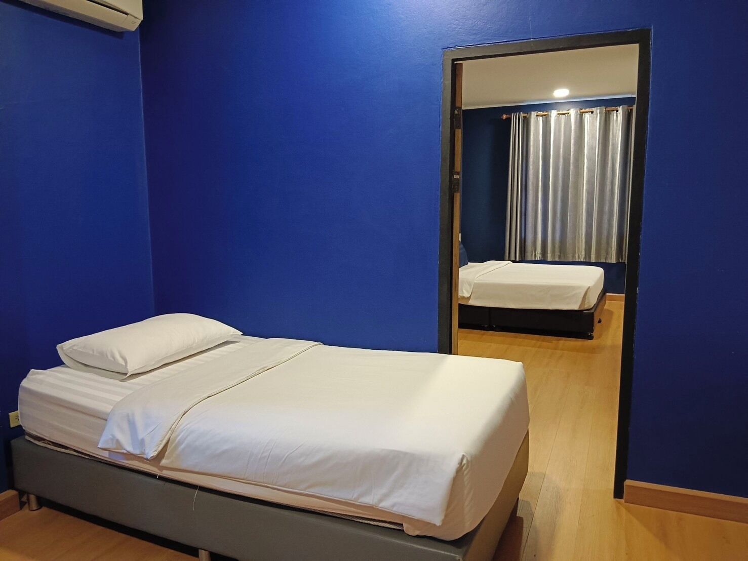 Una cama individual con ropa de cama blanca en una habitación con paredes azules y piso de madera.