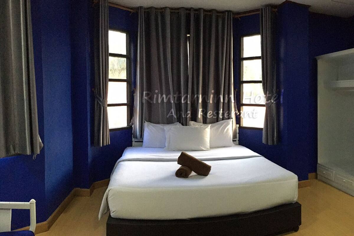 Habitación de hotel con una cama grande, dos ventanas con cortinas, un armario y una pequeña mesa.