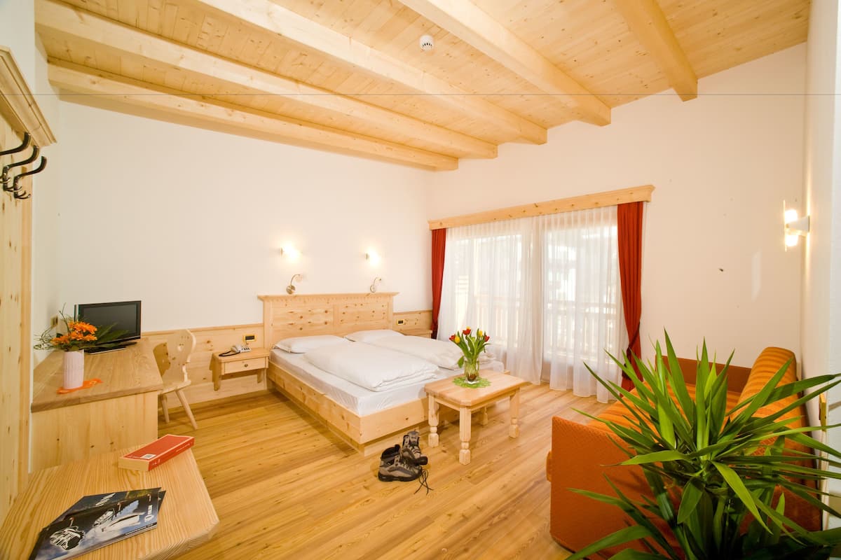 A wooden-floored room with a bed, a desk, a chair, and a plant.