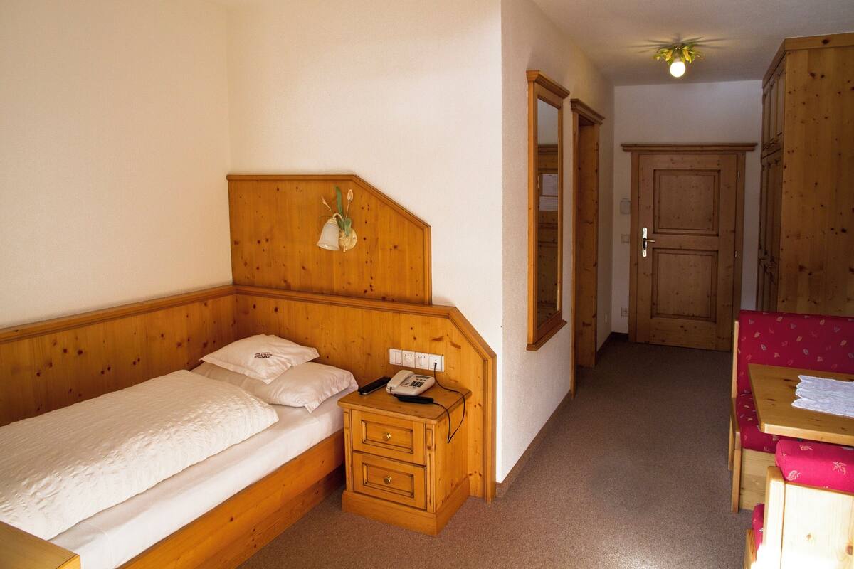 A wooden bed with a nightstand, a telephone, and a wall-mounted light fixture.