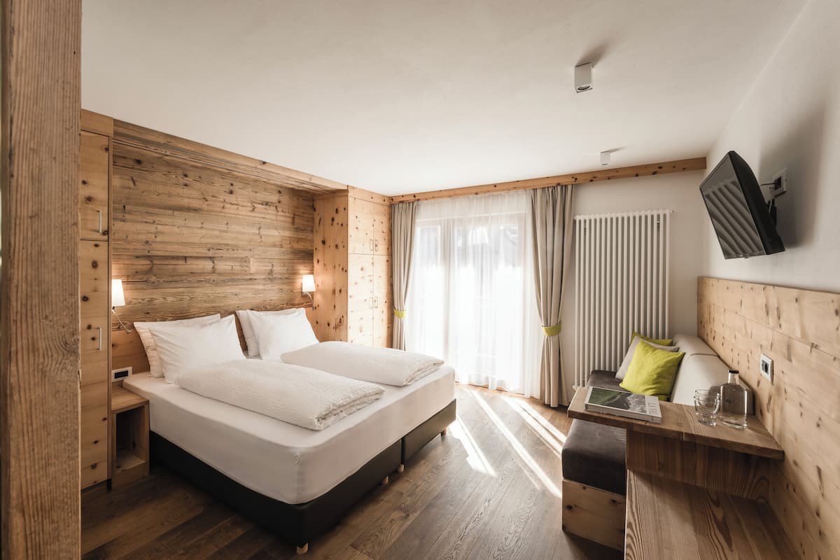 A modern bedroom with a wooden headboard, a bed with white linens, a bedside table with a lamp, and a TV mounted on the wall.