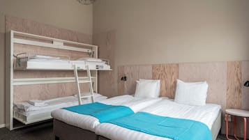 Una habitación de hotel con una cama individual, una litera, una mesita pequeña y un estante fijado a la pared.