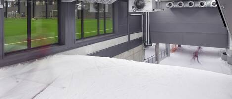 Un espacio interior cubierto de nieve con ventanas grandes, un ventilador y vistas a un campo verde.