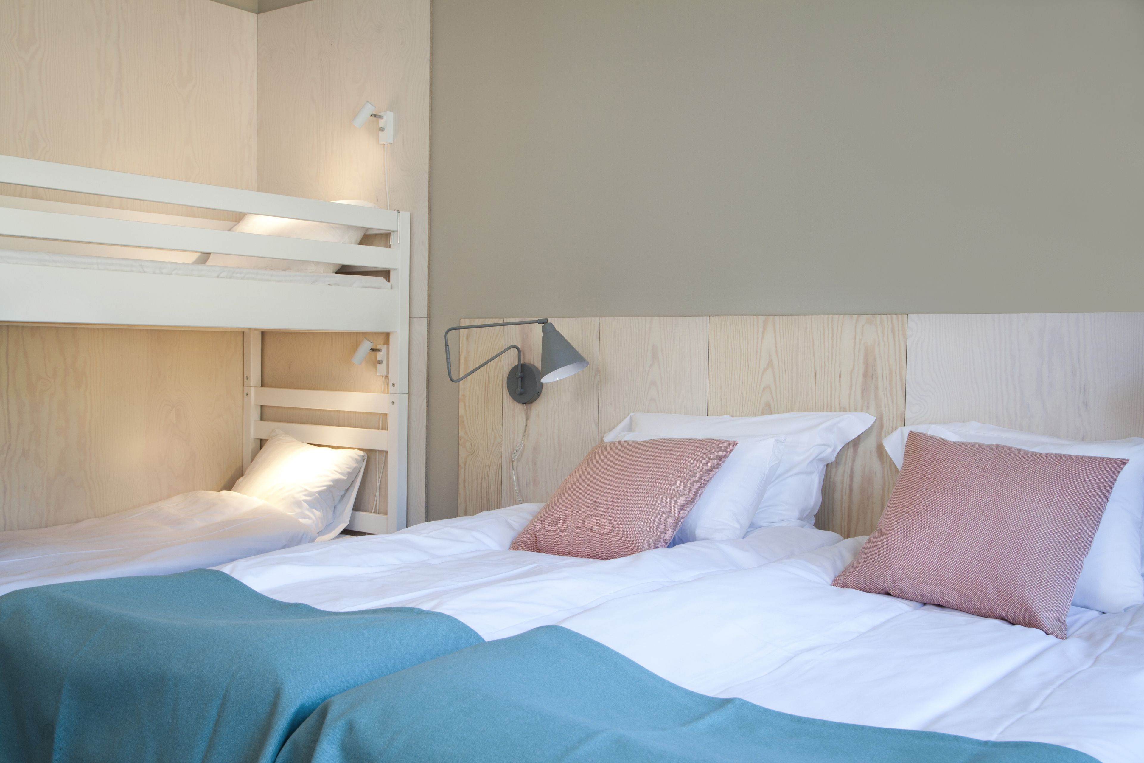 Una litera con una cama inferior y una cama individual, ambas con ropa de cama blanca y almohadas rosas.