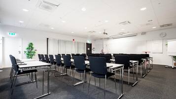 A conference room with multiple tables and chairs, white walls, and a clock on the wall.