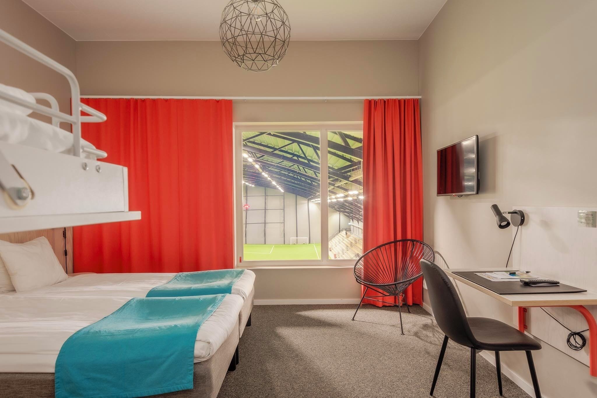 Una habitación de hotel con una cama, un escritorio con silla, un televisor y una ventana con cortinas rojas.