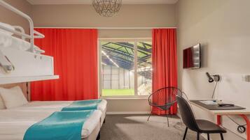 Una habitación de hotel con una cama, un escritorio con silla, un televisor y una ventana con cortinas rojas.
