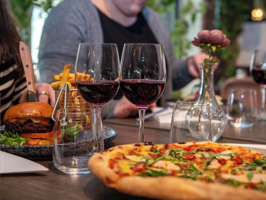 A dining table with a burger, fries, pizza, and wine glasses.