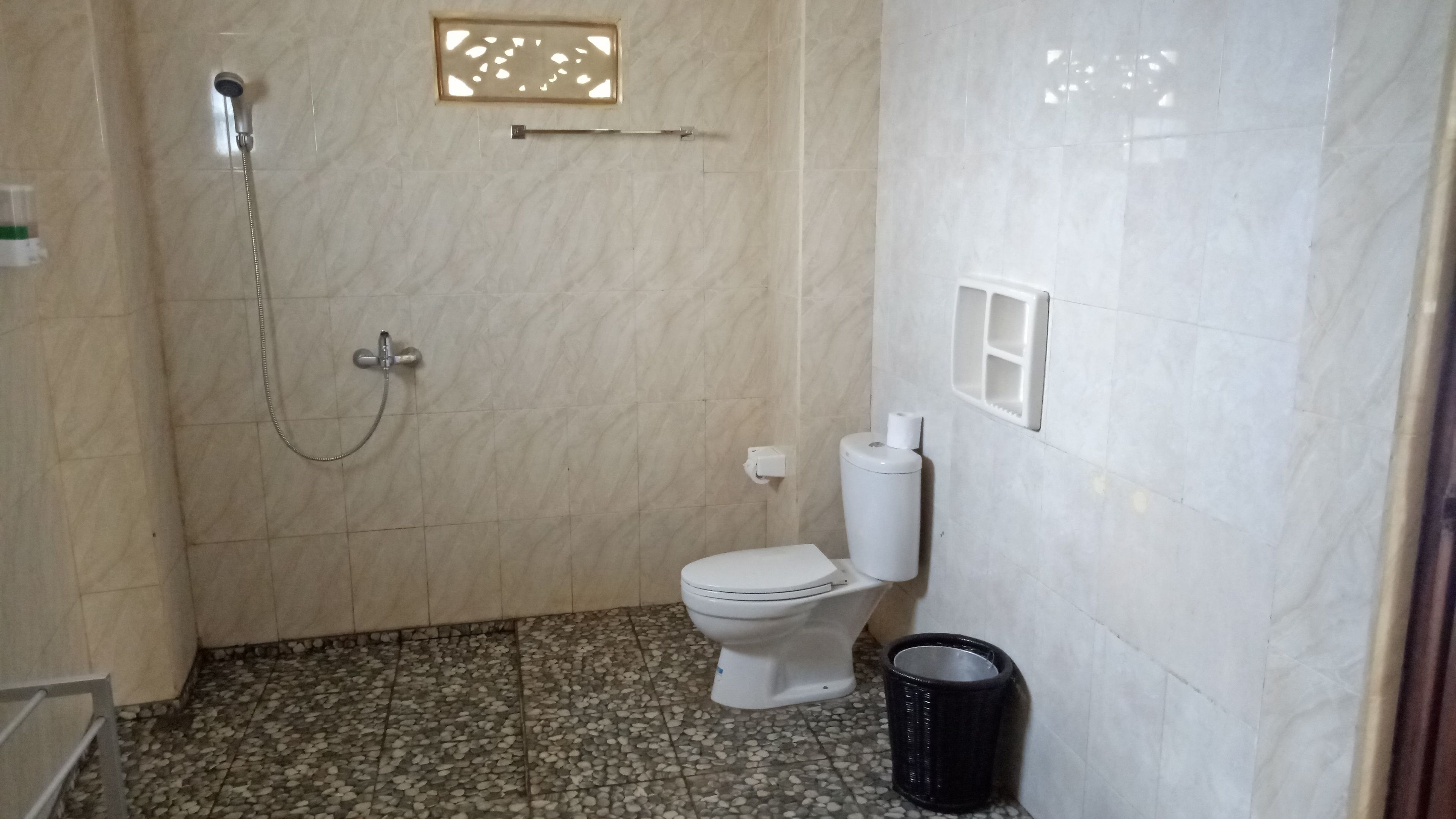 A bathroom with a shower, toilet, and a trash bin.