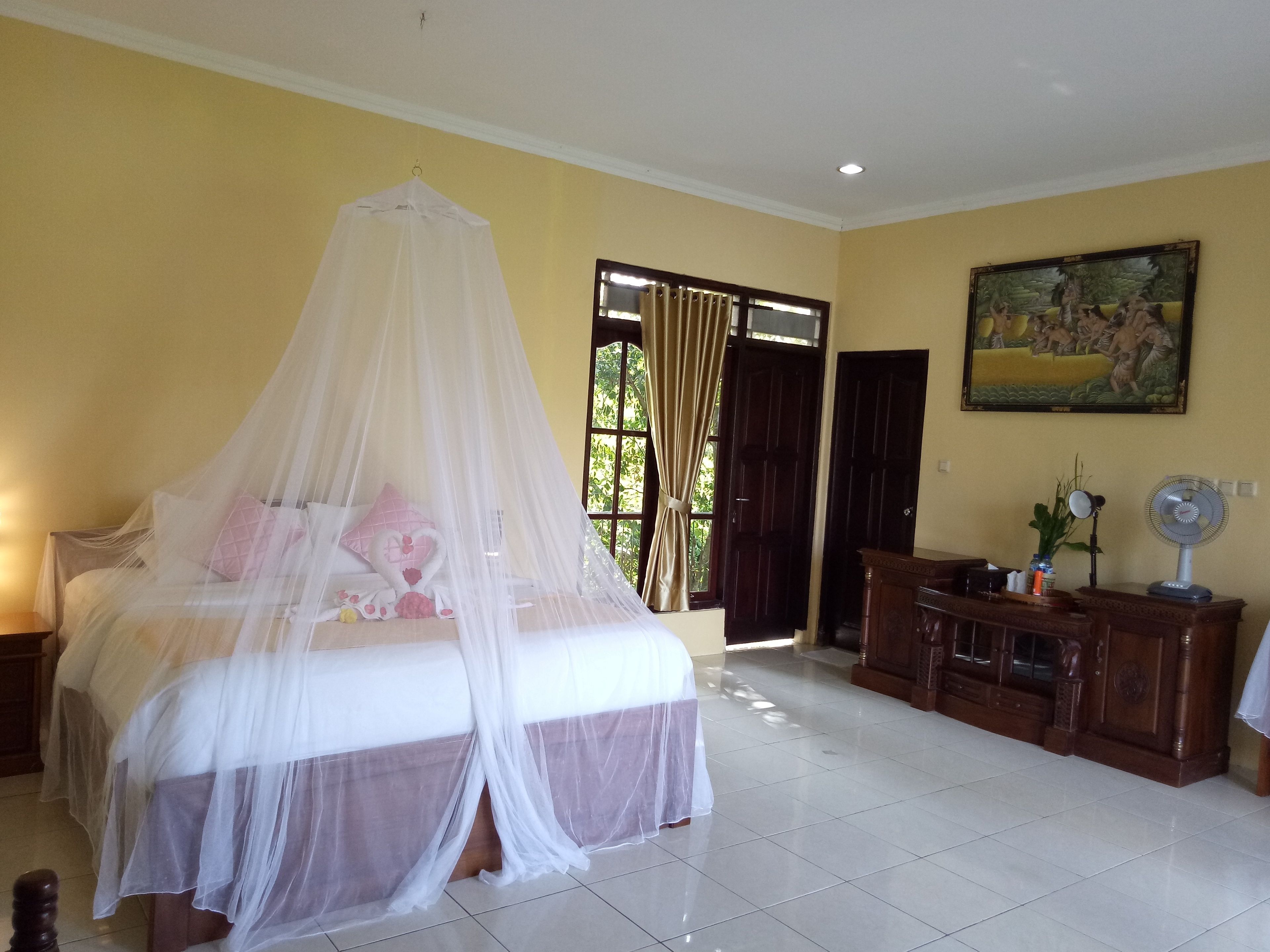 A bedroom with a bed covered by a white canopy, a wooden dresser, and a painting on the wall.
