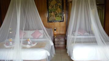 Two beds with white bedsheets and pink pillows, each with a canopy. There is a wooden nightstand between the beds.