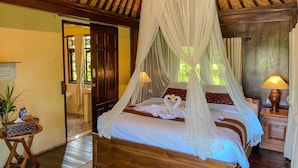 Un dormitorio con cama de dosel, suelo de madera, una mesita de noche pequeña y una mesita con lámpara.