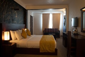 Una habitación de hotel con una cama grande, lámparas de noche, televisión y un escritorio con cafetera.