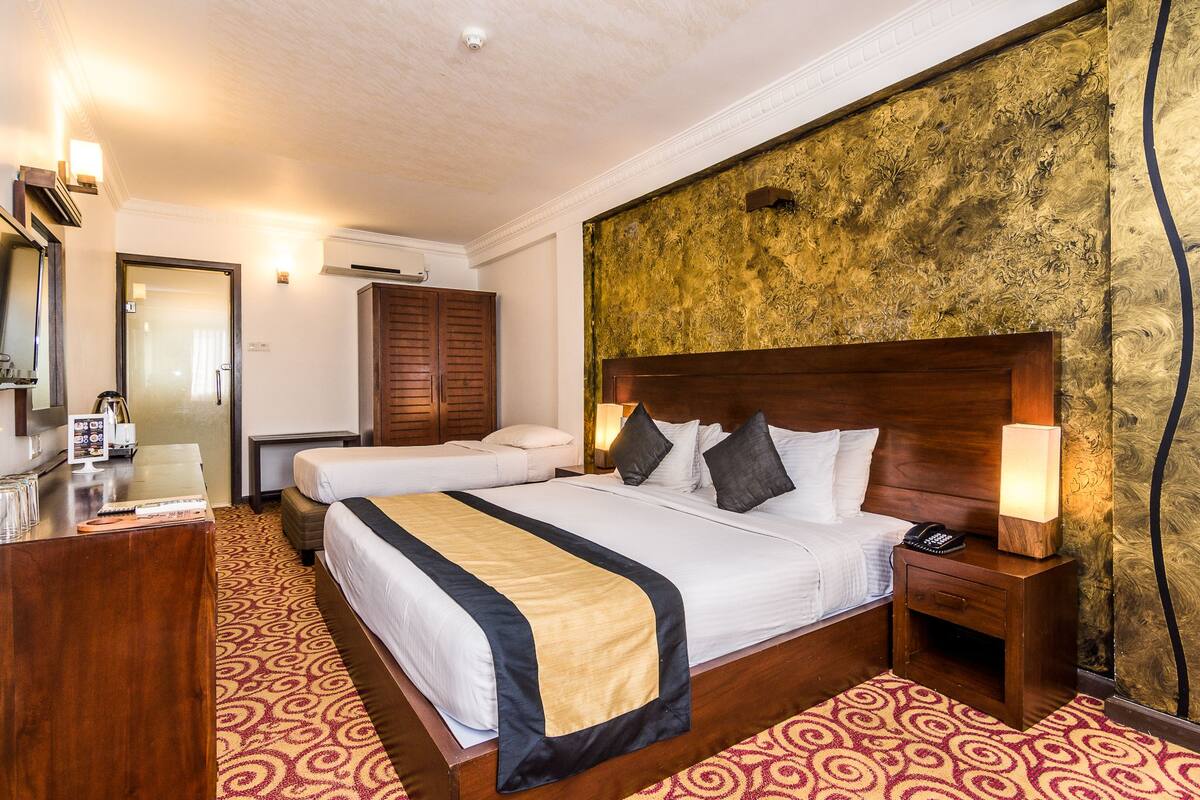 Quarto de hotel com uma cama grande, uma cama menor, uma escrivaninha com telefone e um espelho.