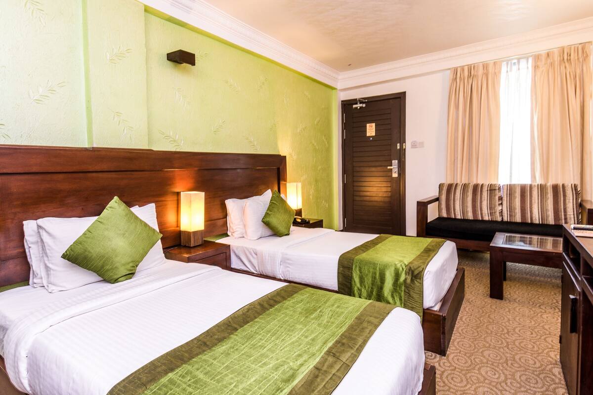 Quarto de hotel com duas camas, um sofá, uma escrivaninha e uma porta.