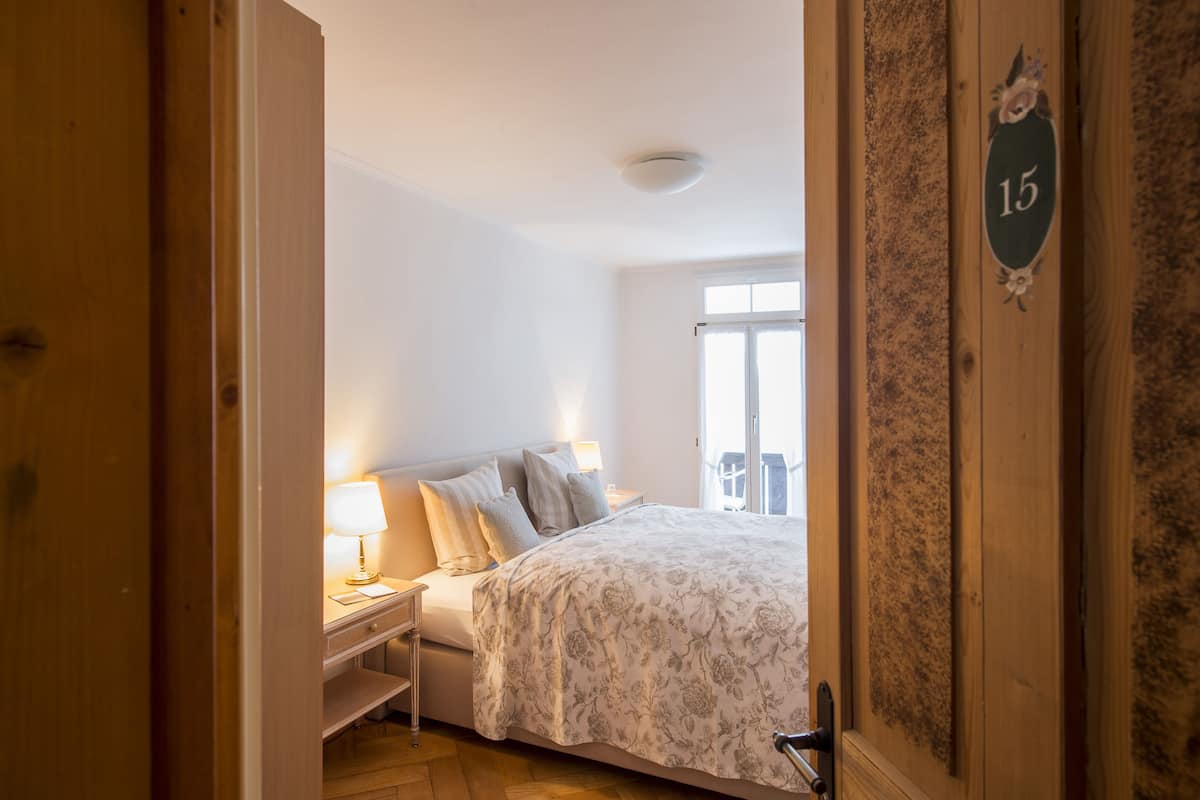 A bedroom with a bed, nightstand, lamp, and a window with a view.