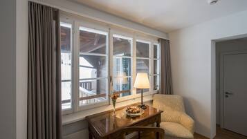 Una habitación con escritorio de madera, una silla, una lámpara y una ventana con cortinas.