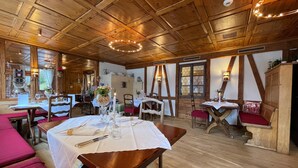 Restaurant amb bigues de fusta al sostre, taules cobertes amb teles blanques i seients amb coixinets vermells.