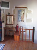 A room with a wooden desk, a chair, a television mounted on the wall, a painting, and a fire extinguisher.