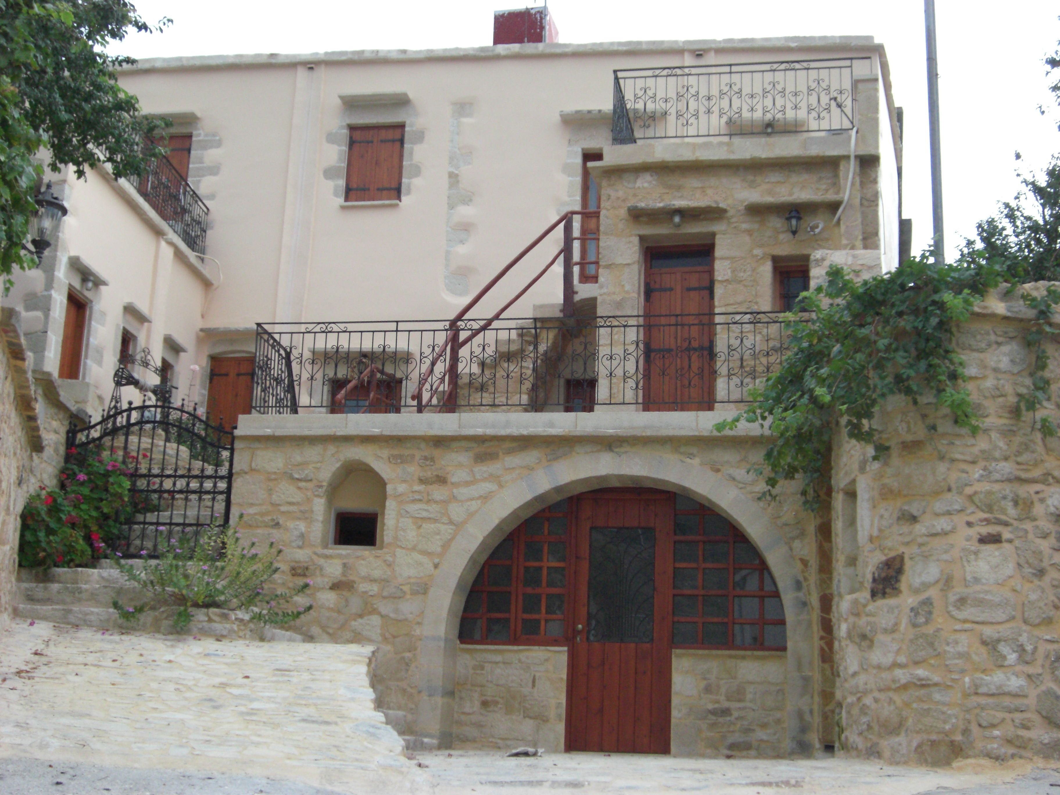 A stone building with a central arched doorway, a staircase leading to a balcony, and a small window on the upper floor.