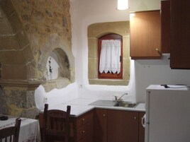 A small kitchen with stone walls, a wooden cabinet, a window with a curtain, and a sink.