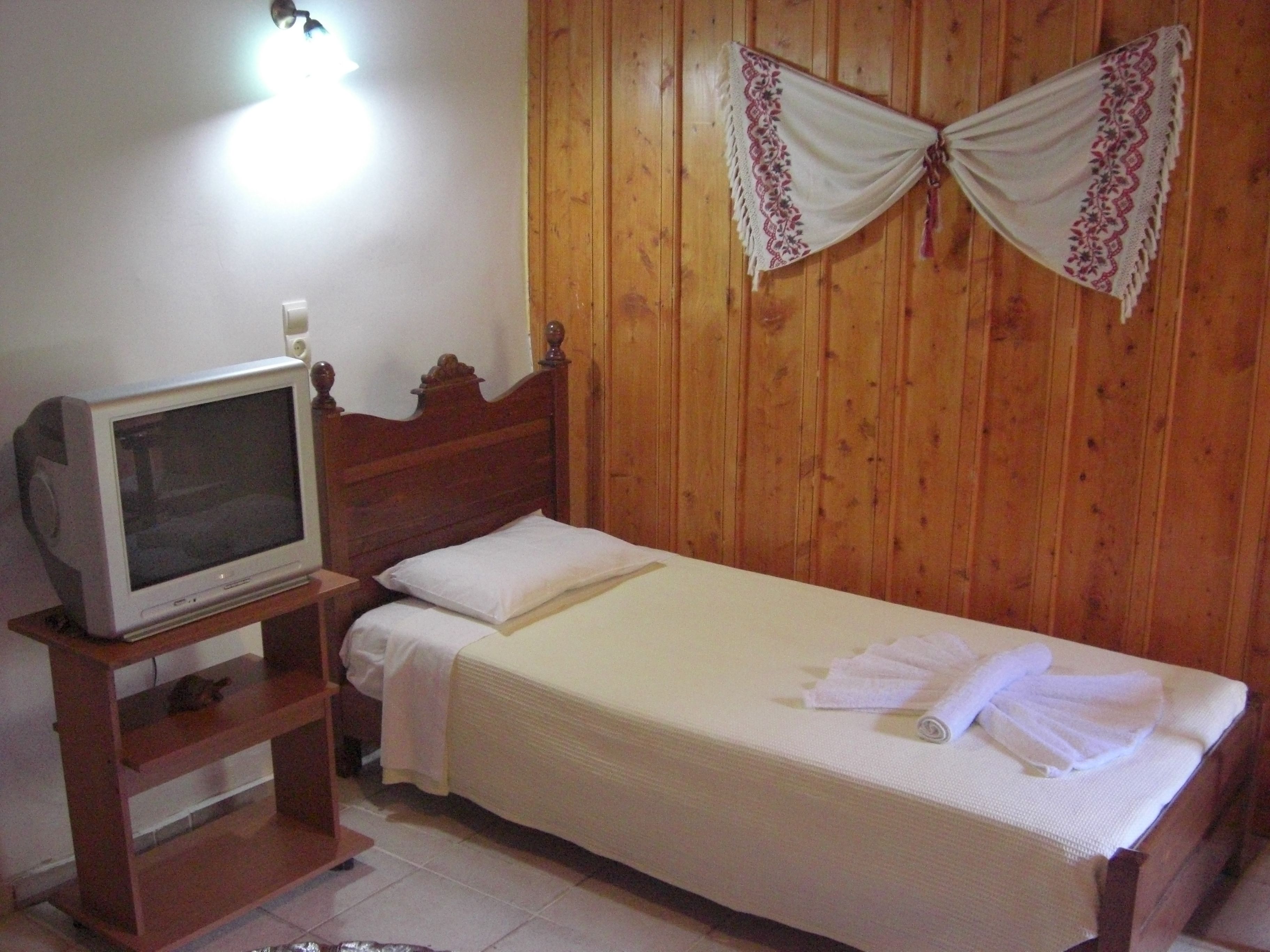 Une chambre à coucher avec une tête de lit en bois, un téléviseur posé sur un meuble en bois, et un lit recouvert de draps et de serviettes blancs.