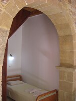 A small, single-bed room with a wooden headboard, a white mattress, and a white blanket.