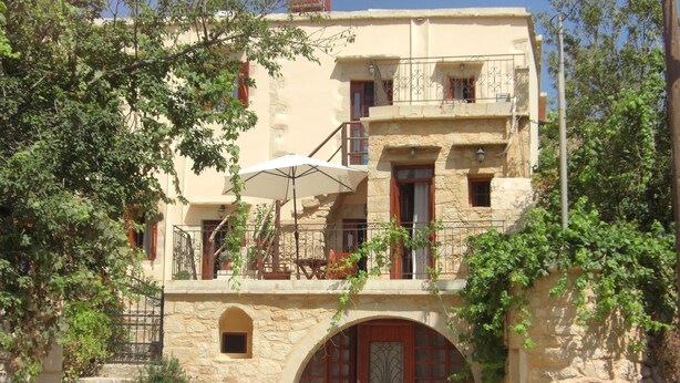 A stone building with a central archway, multiple balconies, and a large umbrella. - Patriko Traditional Residence (Apokoronas)