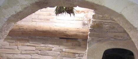 Une cheminée en pierre avec un manteau en briques, une petite étagère ornée d’objets décoratifs et un arc en pierre au-dessus.