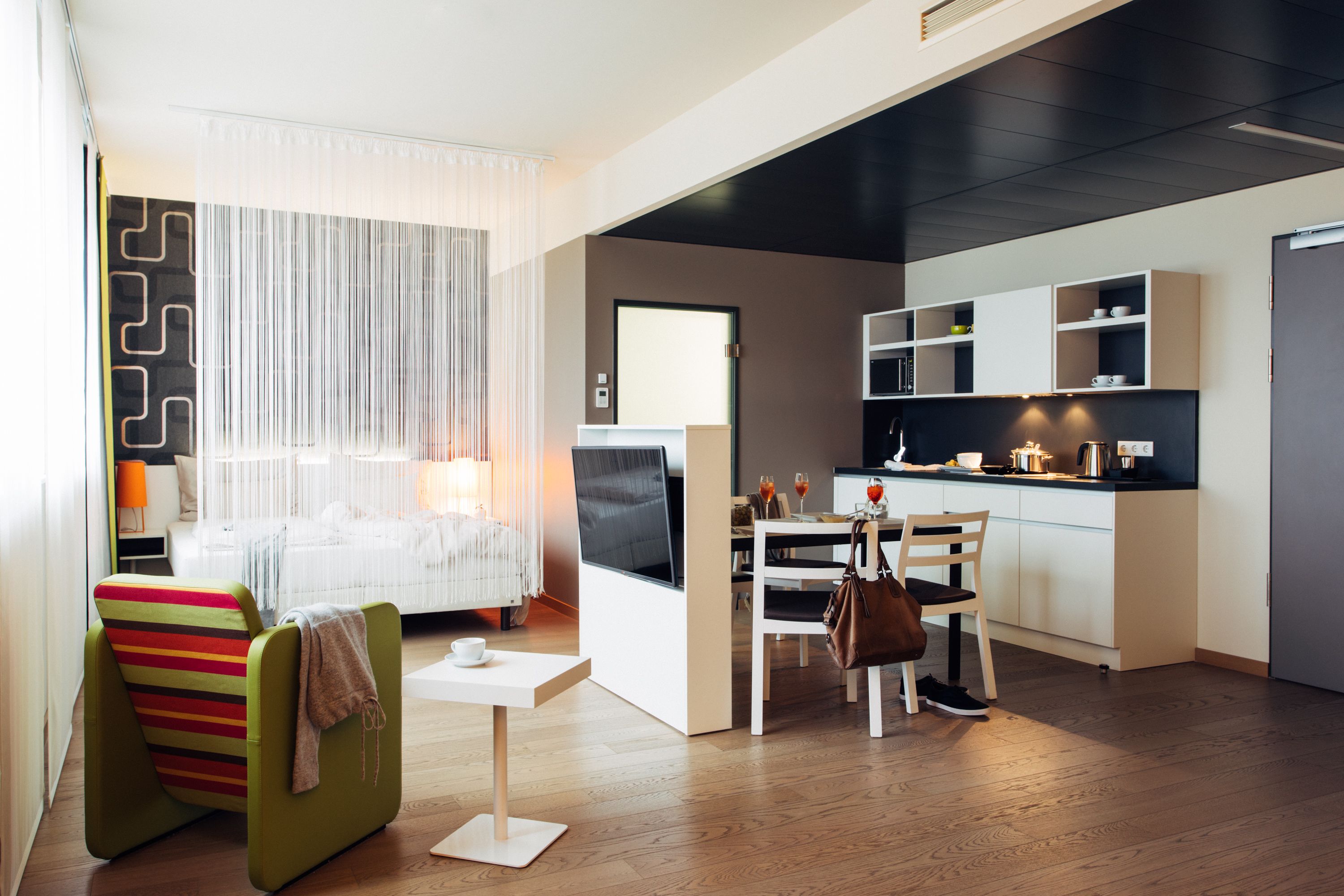 Quarto de hotel moderno com cama, área de refeições, cozinha e sala de estar.