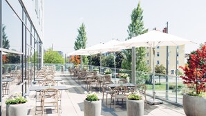 An outdoor patio with tables and chairs, large umbrellas, and potted plants. - harry’s home München Moosach hotel & apartments (Munich)