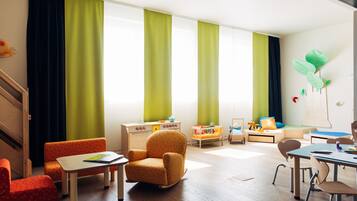 A children's playroom with a wooden floor, a rocking chair, a small table, and a play area with toys and a sofa.