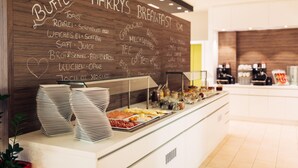 A breakfast buffet counter with a wooden board displaying food options and a glass display case with various food items. - harry’s home München Moosach hotel & apartments (Munich)
