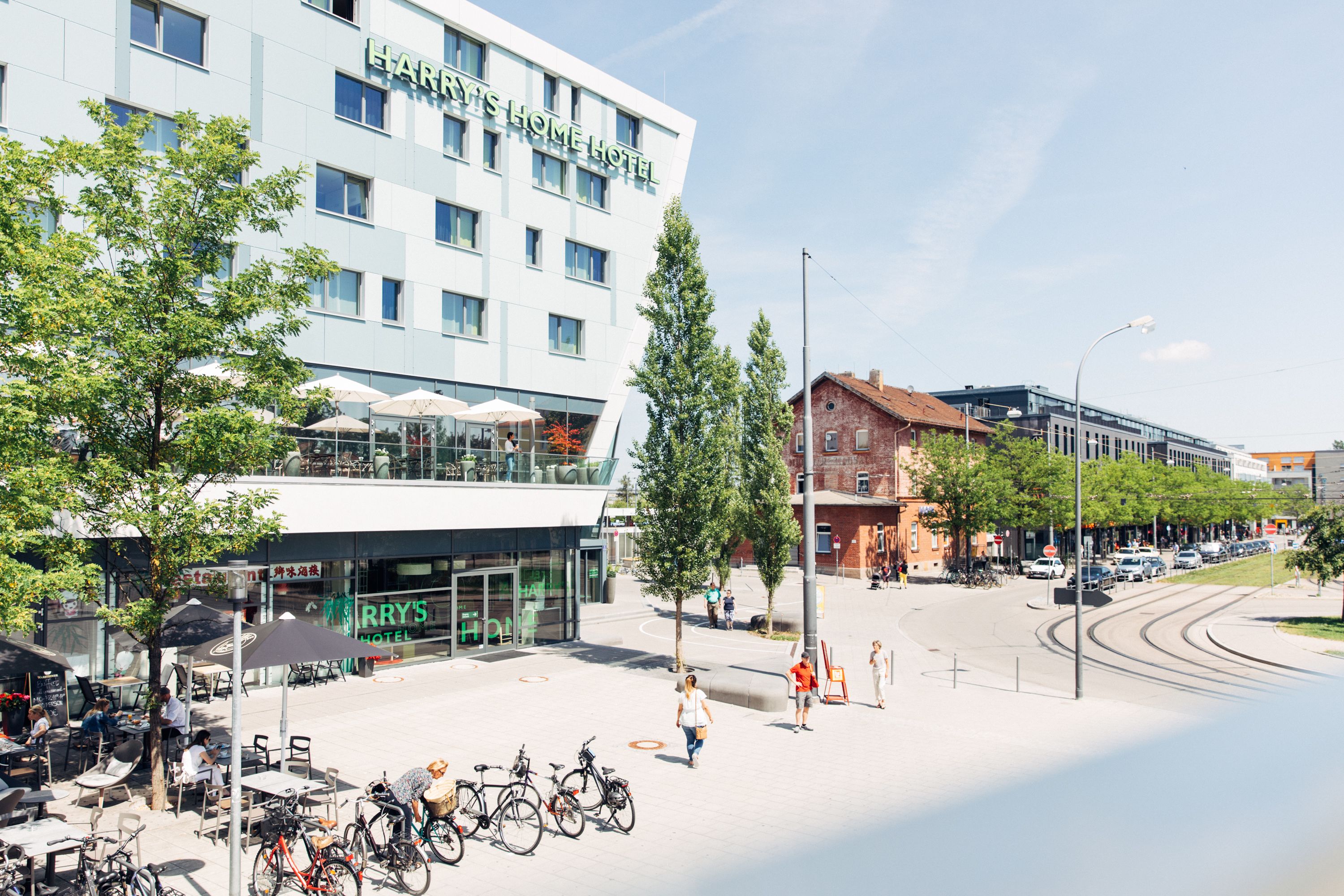 Un hotel moderno con fachada de vidrio, zona de estar al aire libre y bicicletas estacionadas afuera.