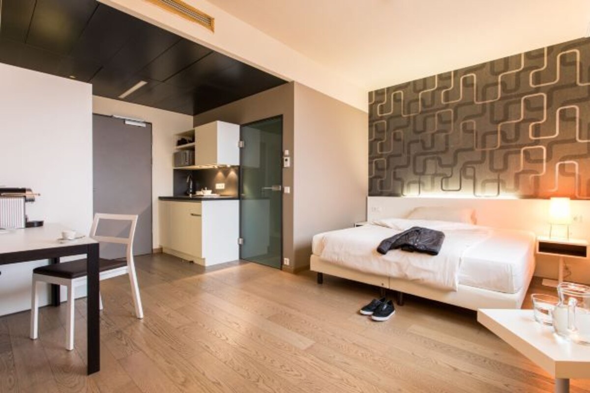 Una habitación de hotel moderna con cama, escritorio, silla y kitchenette.