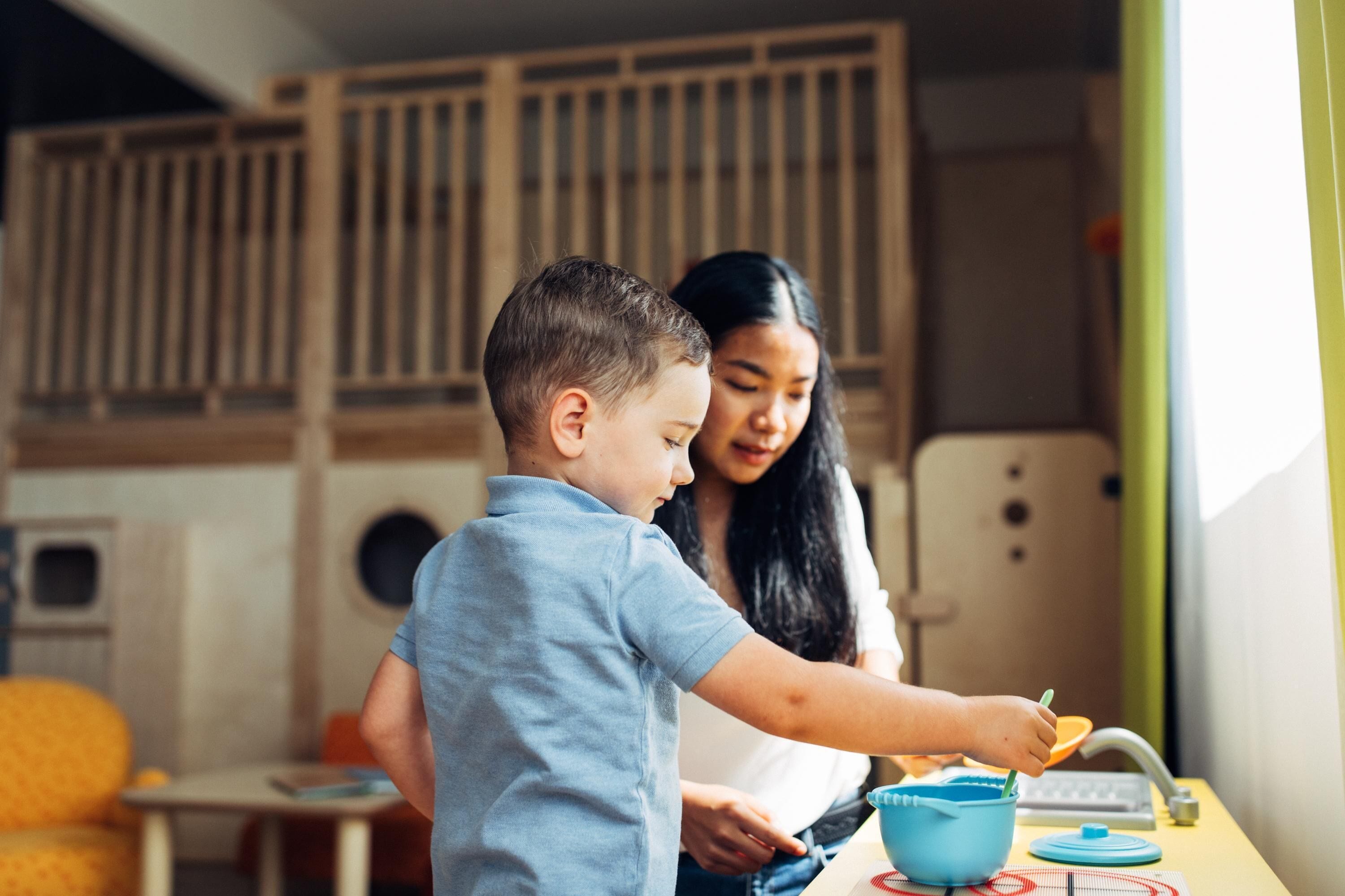 Un niño y un adulto en una encimera de cocina, con un tazón y una cuchara, un teclado y una ventana con cortinas.