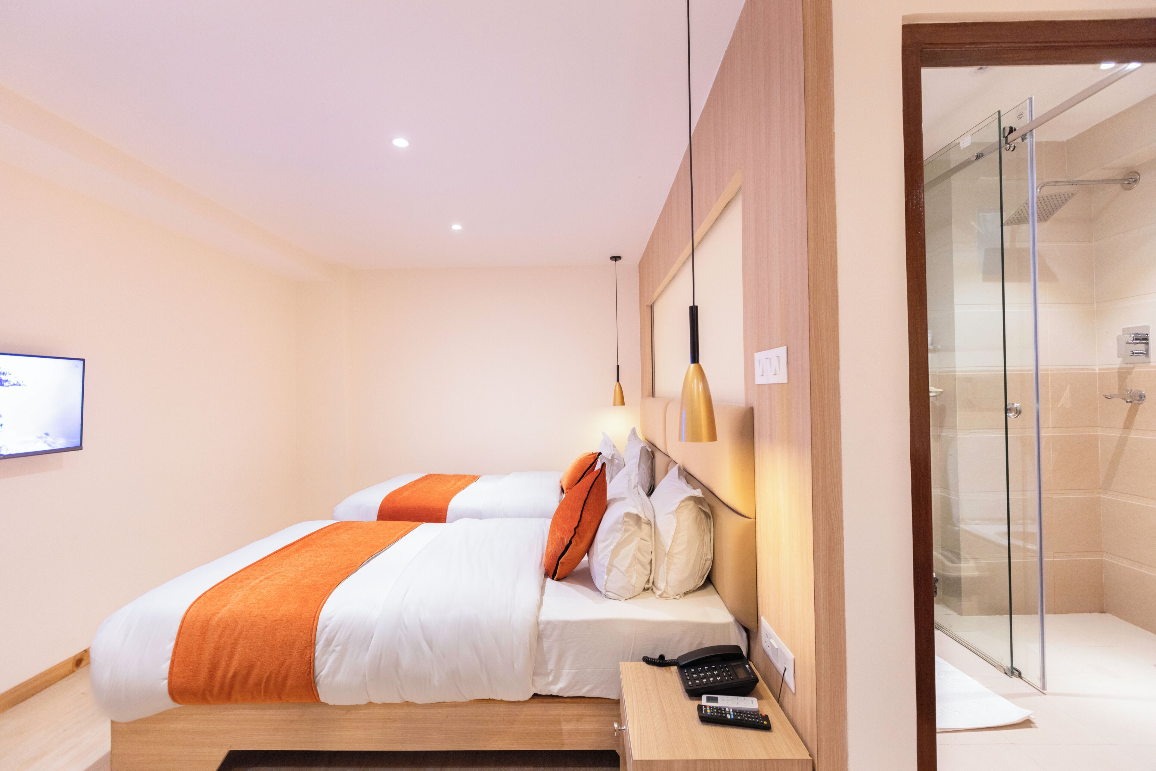 A hotel room with two beds, a shower area, and a mounted television.