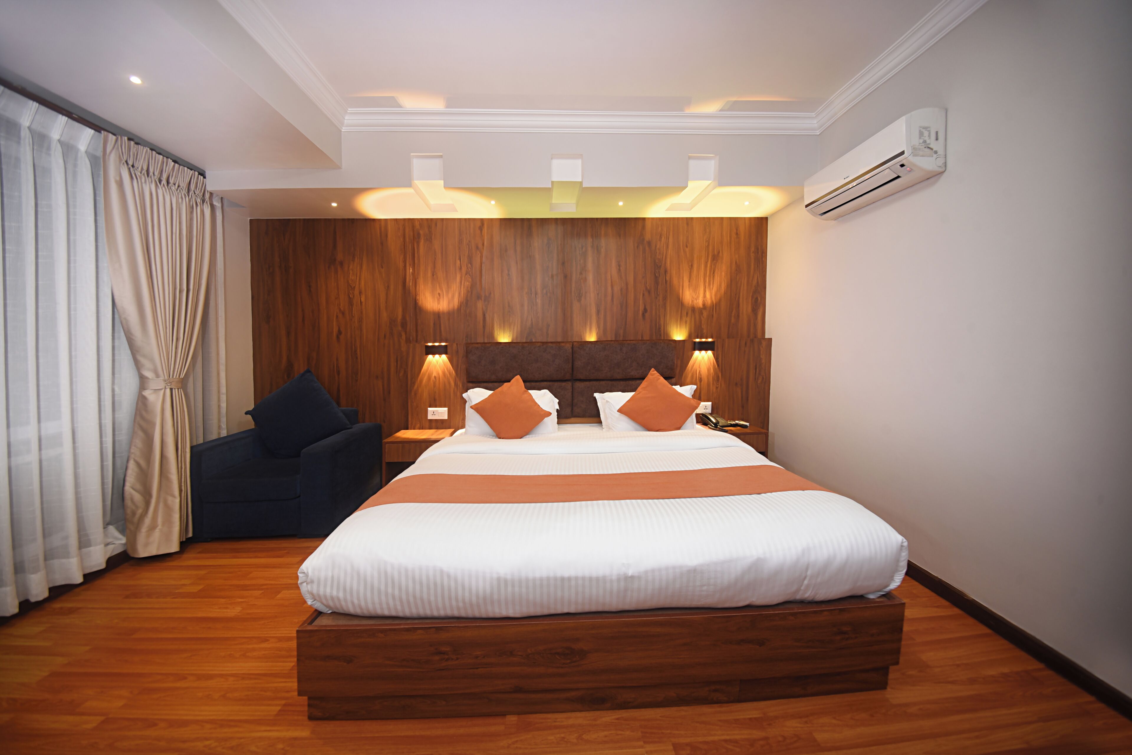 A modern hotel room with a large bed, wooden headboard, and a dark blue armchair.