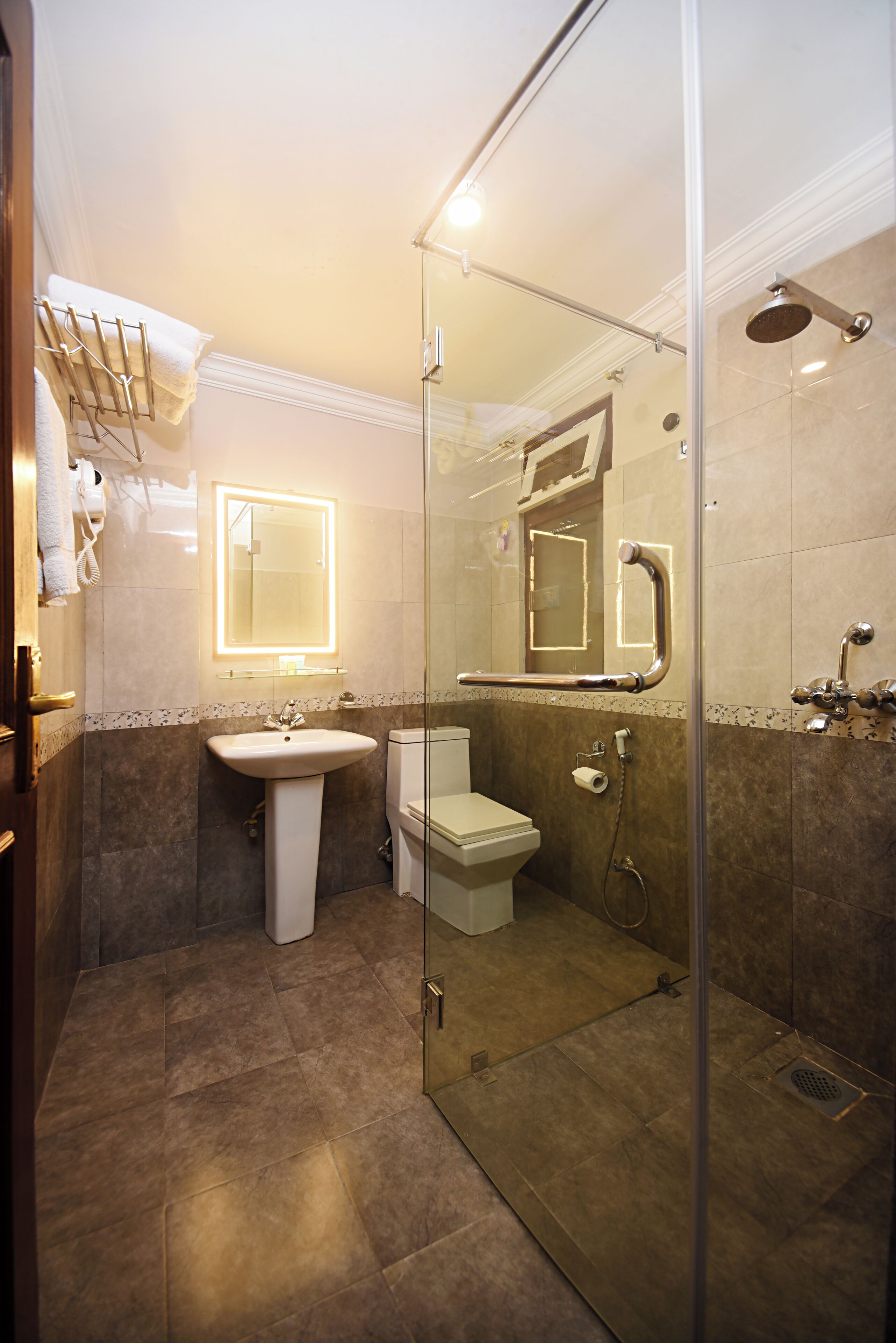 A modern bathroom with a glass-enclosed shower, a pedestal sink, a toilet, and a mirror with a lighted frame.