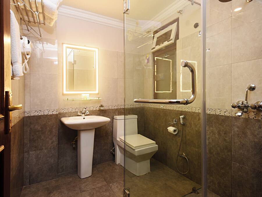 A modern bathroom with a glass-enclosed shower, a pedestal sink, a toilet, and a mirror with a lighted frame.
